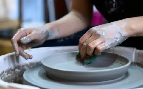 Mani sporche di argilla lavorano su un piatto al tornio, creando forme uniche con lavori con argilla senza cottura.