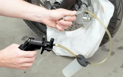 Ręce majsterkowicza odkręcają odpowietrznik zacisku hamulcowego, przygotowując się do tego, jak wymienić płyn hamulcowy w motocyklu.