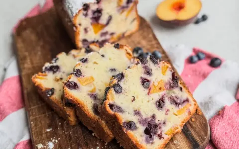 Saftiger Joghurt Kuchen mit Blaubeeren und Pfirsichstücken, bestäubt mit Puderzucker.