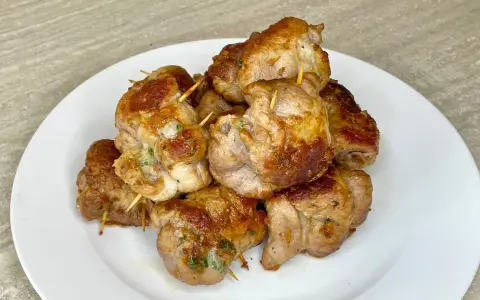 Un mucchio di bombette pugliesi ricetta, dorate e succulente, tenute insieme da stuzzicadenti, su un piatto bianco.