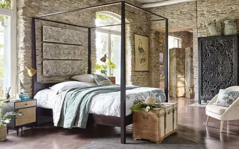 Ein Schlafzimmer mit Steinwänden und einem Himmelbett. Drei Wandpaneele mit orientalischen Mustern hängen über dem Bett. Ein Holztruhe steht am Fußende.