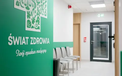Zielona ściana z napisem "Świat Zdrowia", rząd krzeseł i drzwi w poczekalni kliniki.