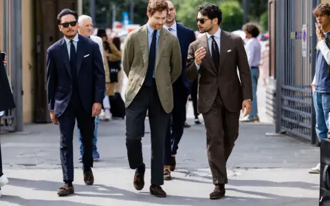 Trzech mężczyzn w eleganckich garniturach i stylowych loafersach do garnituru idzie ulicą.
