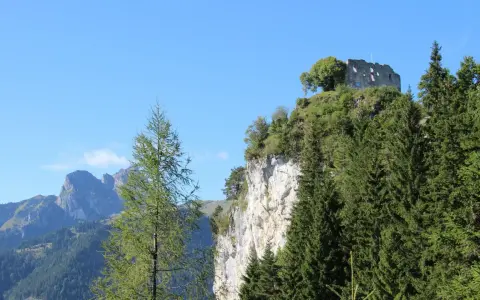 Burgruine Falkenstein thront auf Felsklippe, umgeben von Nadelbäumen. Perfekt für eine Wanderung mit Bergblick.