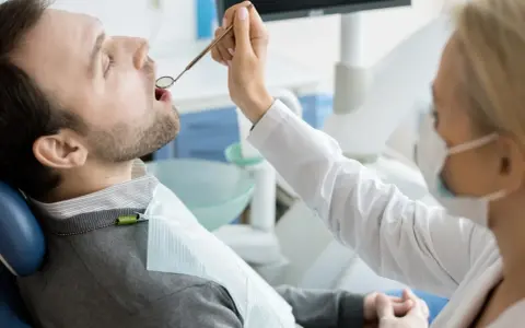 Pacjent u dentysty, zastanawia się, ile kosztuje wizyta u dentysty prywatnie. Lekarz bada jego zęby.