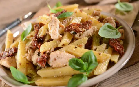 Penne z kurczakiem i suszonymi pomidorami, ozdobione świeżą bazylią. Pyszne danie, które zachwyci każdego smakosza.