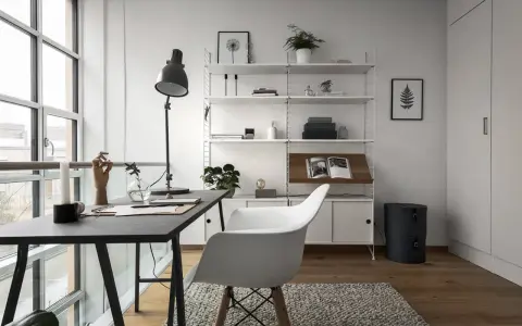 Ett modernt hemmakontor med ett mörkt skrivbord, en vit stol och en stilren, inredd bokhylla. Ljuset flödar in från stora fönster.