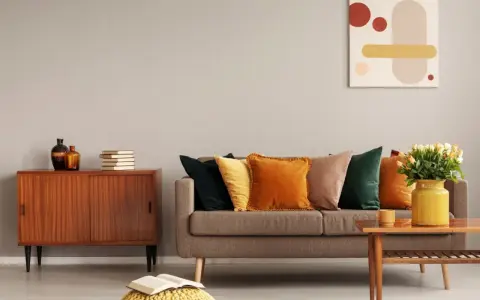 Un salon cosy aux couleurs automnales, avec un canapé garni de coussins ocre et vert forêt, un meuble vintage en bois et une peinture abstraite.