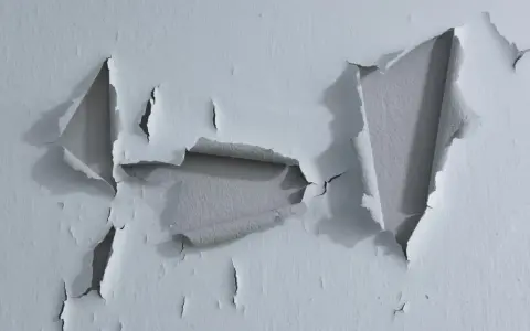 Pintura desconchada revela capas de color gris bajo la superficie blanca.