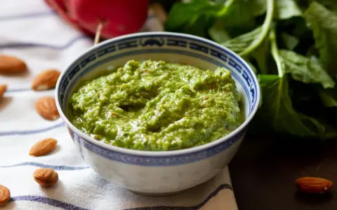 Zielone pesto z liści rzodkiewki, z migdałami i świeżymi liśćmi w tle. Idealne do makaronu lub jako dodatek do kanapek.