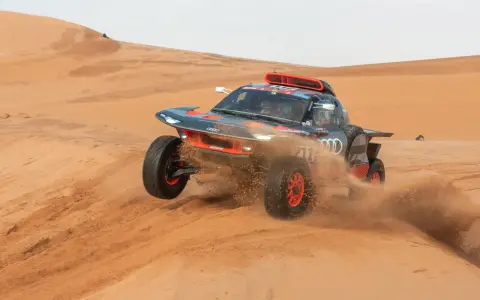 Un'auto da rally Audi sfreccia tra le dune, sollevando sabbia. Un'emozionante tappa del percorso Parigi-Dakar.