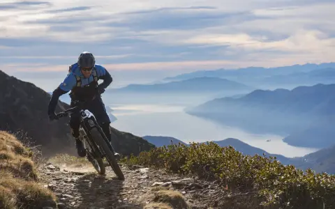 Ein Mountainbiker auf einer abenteuerlichen Tour in den Alpen, mit einem See und Bergketten im Hintergrund.