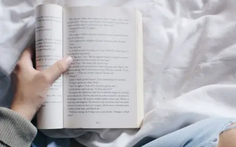 Mano sosteniendo un libro abierto con relatos cortos para mujeres. La página muestra texto y el número 157.