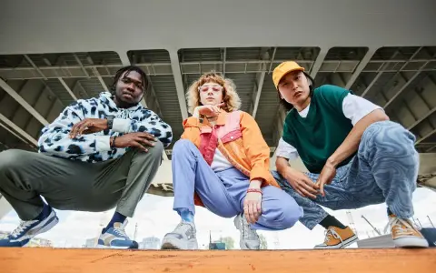 Tre giovani con look urbani, ognuno con le sue sneakers, mostrano cosa sono le sneakers: calzature comode e alla moda per ogni stile.