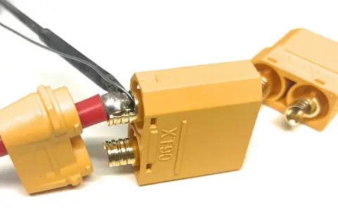 Löten eines roten Kabels an einen goldenen XT90-Stecker. Ein weiterer Stecker liegt daneben.