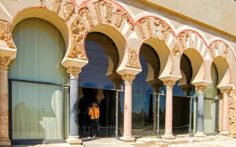 Verzierte Bögen und Säulen der Medina Azahara spiegeln sich in Glas. Besucher bestaunen die historische Architektur.