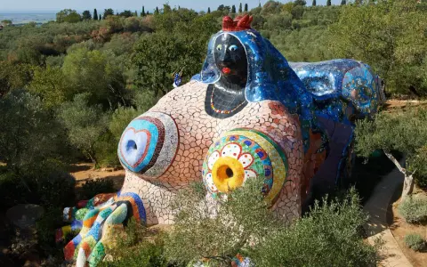 Œuvres d'art de Niki de Saint Phalle : une sculpture monumentale et colorée, représentant une femme allongée, ornée de mosaïques vives, dans un paysage verdoyant.