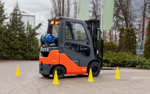 Pomarańczowo-szary wózek widłowy Toyota z butlą gazową, otoczony żółtymi pachołkami, gotowy do testów UDT.