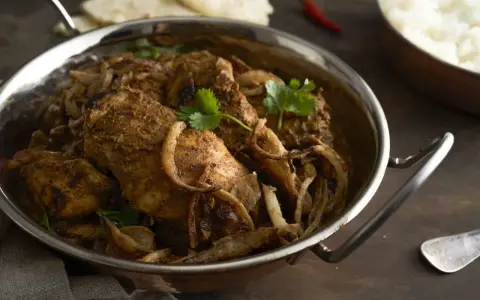 Kurczak w sosie garam masala z cebulą i kolendrą w metalowej misie.