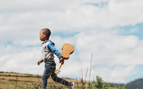 Kleines Kind, 17 Monate, sehr anstrengend, rennt mit Ukulele über Feld.