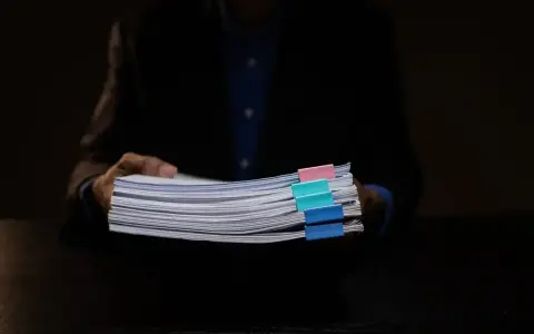 Mężczyzna w garniturze trzyma stos dokumentów z kolorowymi spinaczami. Może to być materiał dowodowy w sprawie hipoteka przymusowa.