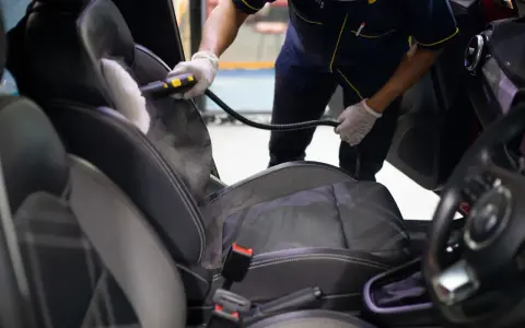 Un profesional usa vapor para limpiar los asientos del coche, mostrando cómo limpiar los asientos del coche de forma efectiva.