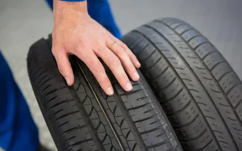 Dłoń mechanika dotyka bieżnika opony Hankook, sprawdzając jej stan. Dobre opony Hankook opinie to podstawa bezpiecznej jazdy.