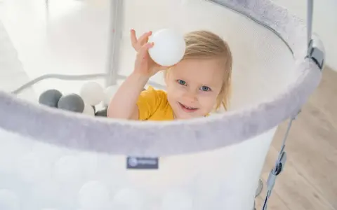Uśmiechnięte dziecko bawi się w basenie z piłeczkami. To świetne ćwiczenia na czucie głębokie dla dzieci, rozwijające zmysły i koordynację.