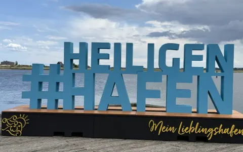 Große blaue Buchstaben mit #Heiligenhafen auf einem Holzpodest. Perfekt für Ausflugsziele und Erinnerungen an diesen schönen Ort.