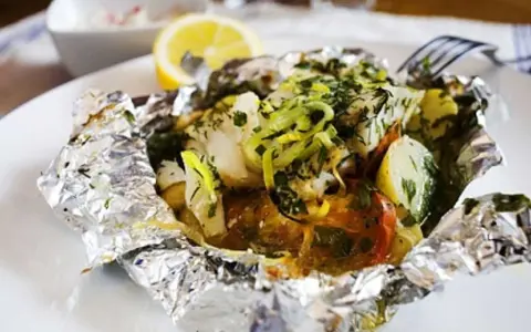 En läcker fiskpaket i ugn med potatis, tomat och örter, toppad med citron och purjolök. Enkel och smakrik middag.