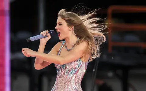 Taylor Swift w błyszczącej sukience śpiewa na koncercie w Warszawie, włosy rozwiane przez wiatr.
