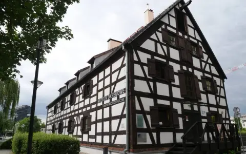 Stary, biały spichlerz z ciemnymi belkami, mieszczący Muzeum Okręgowe. Widać schody prowadzące do wejścia i drzewa w pobliżu.