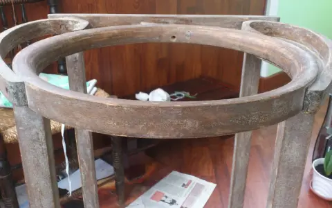 Estructura de madera de un palanganero antiguo, lista para restaurar. Se aprecian sus patas y el aro superior curvo.