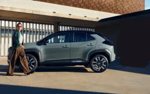 Stylowa kobieta w luźnych spodniach i zielonej kurtce idzie obok swojego nowego, miejskiego auta. Idealne auto dla kobiety, które podkreśla jej indywidualność.