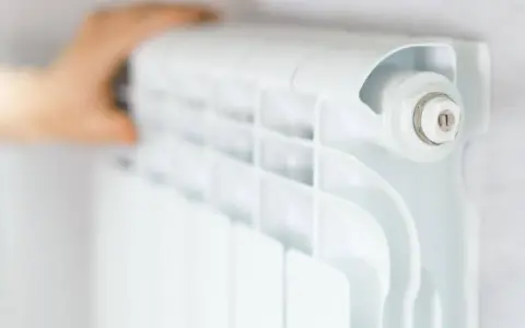 Main d'une personne ajustant un radiateur blanc, élément clé du système chauffage maison.