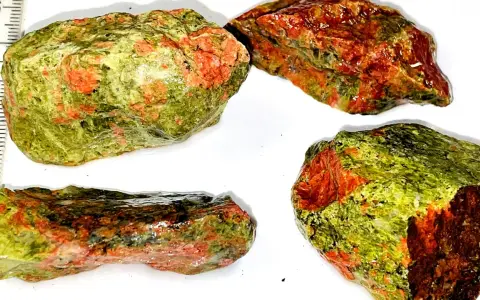 Quattro pezzi grezzi di unakite, con le loro vibranti sfumature verdi e rosse, mostrano le loro proprietà naturali.