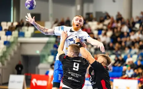 Jakub Wolski w akcji, walczy o piłkę w powietrzu z dwoma przeciwnikami.