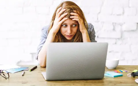 Verzweifelte Frau mit Händen in den Haaren, die auf einen Laptop starrt. Die Website-Migration scheint sie zu überfordern.
