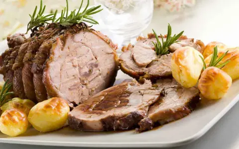 Succulento arrosto di vitello affettato, guarnito con rosmarino e accompagnato da patate arrosto dorate.