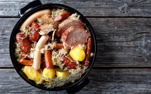 Choucroute garnie, un plat emblématique des alsace spécialités culinaires, avec saucisses, viandes et pommes de terre dans une cocotte.