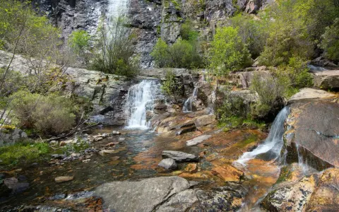 Las chorreras de despeñalagua, cascadas de agua blanca cayendo sobre rocas rojizas y verdes arbustos en un paisaje rocoso.