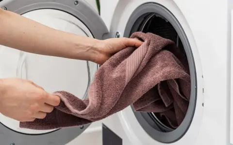 Manos colocando una toalla rosa en una lavadora. Aprende como lavar toallas para que queden suaves y esponjosas.