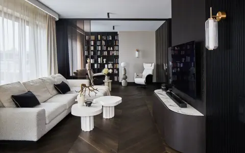 Nowoczesny salon z wygodną sofą, stolikami i regałem pełnym książek. Dominują ciemne, grafitowe akcenty, tworząc elegancką atmosferę.