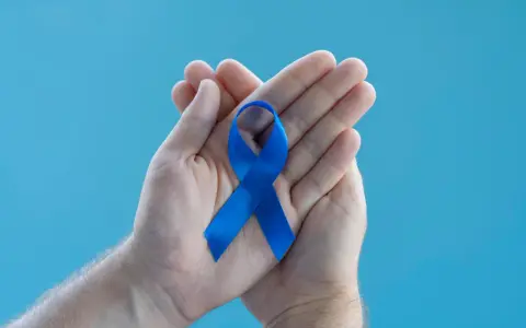 Dłonie trzymające niebieską wstążkę symbolizującą wsparcie dla mężczyzn. Warto poznać domowe sposoby na prostatę.