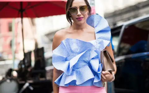 Eleganza in **abbinamento rosa e blu**: top a balze a righe azzurre e bianche con pantaloni rosa cipria, occhiali da sole e borsa a tracolla.