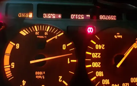 Czerwony wykrzyknik BMW świeci się na desce rozdzielczej, obok wskaźników prędkości i obrotów.