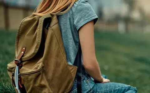 Mädchen mit braunem Rucksack sitzt im Gras. Der Rucksack ist bereit für das Waschen, um ihn wieder frisch zu machen.