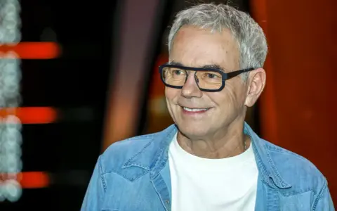 Uśmiechnięty mężczyzna w okularach, w jeansowej koszuli, jakby czekał na pytanie: "Jaka to melodia?".