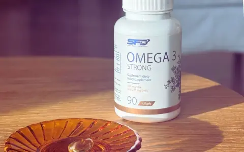 Biała butelka suplementu diety Omega 3 Strong. Na małej, bursztynowej podstawce leży jedna kapsułka. Kwasy omega 3 na co? Na zdrowie!