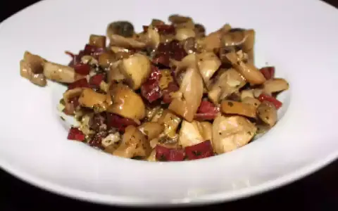 Champiñones salteados con trocitos de jamón, servidos en un plato blanco. Un plato sencillo y sabroso.